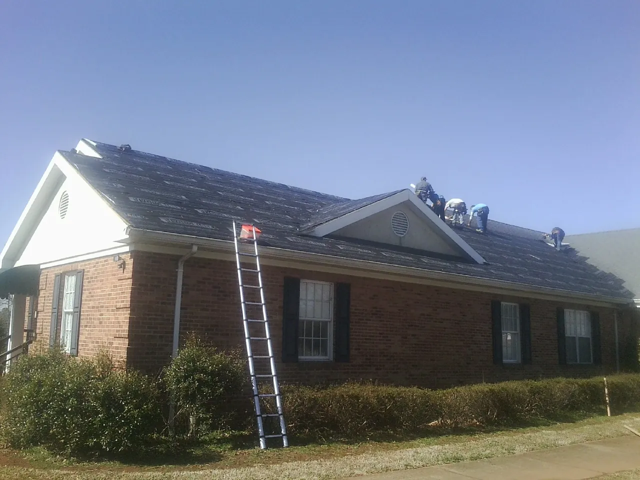 Crew tearing shingles off a brick ranch roof with a ladder set — Metal Roof Repair work by our crew in Lucasville