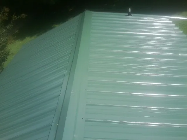 New green metal panels meeting at the ridge of a roof — Flat Roof Repair work by our crew in Lucasville
