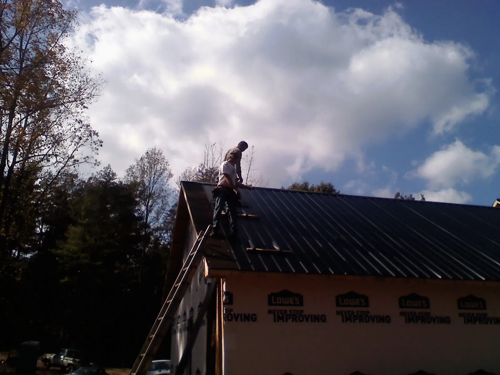 Roofer fastening dark metal panels high against a cloudy sky, from a Roof Inspection job in Lucasville
