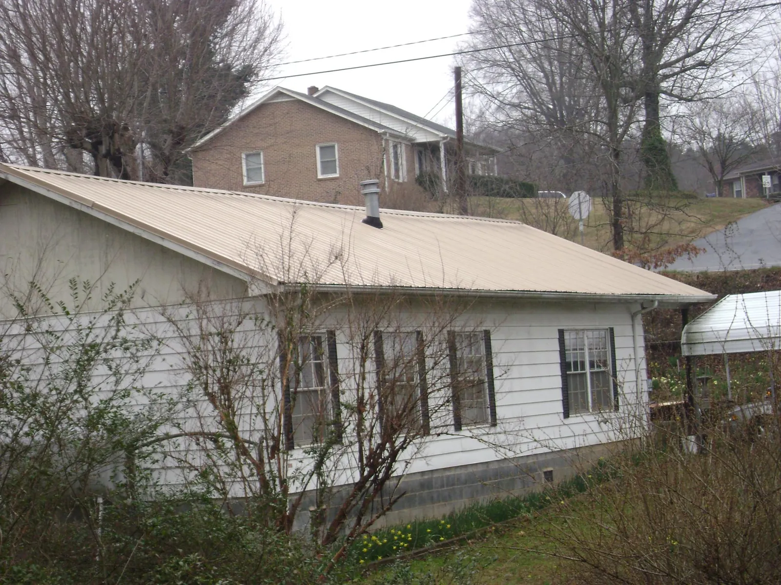 Tan metal roof on a white sided house set into a hillside — Commercial Roofing by Roofing Brothers in Lucasville
